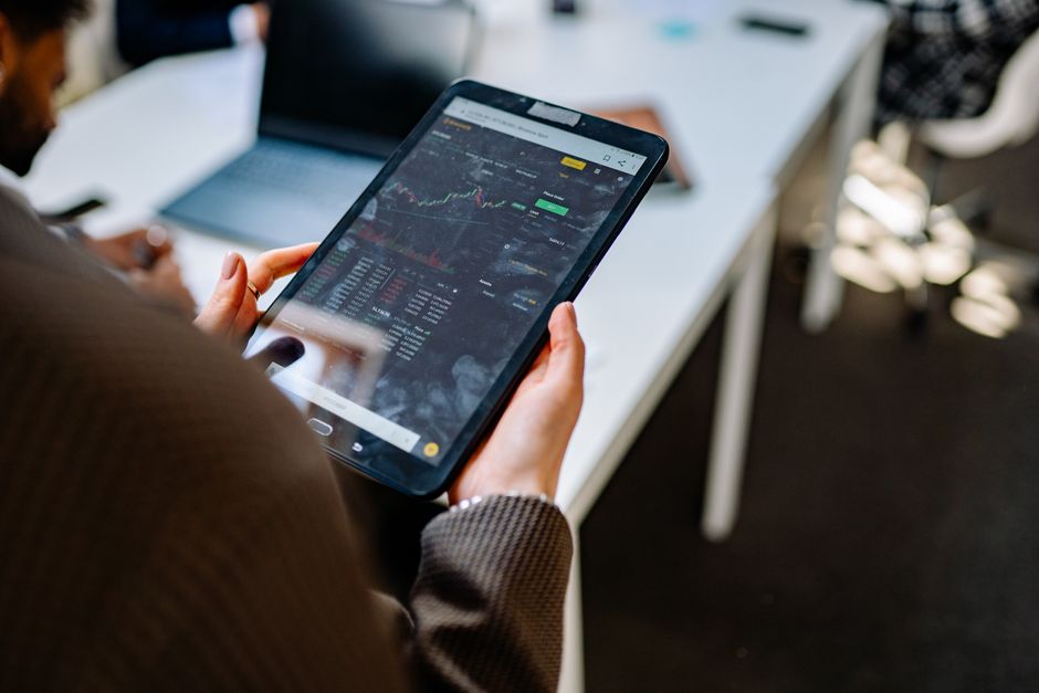 investing in green bonds — A person using a tablet for stock market analysis in an office setting.
