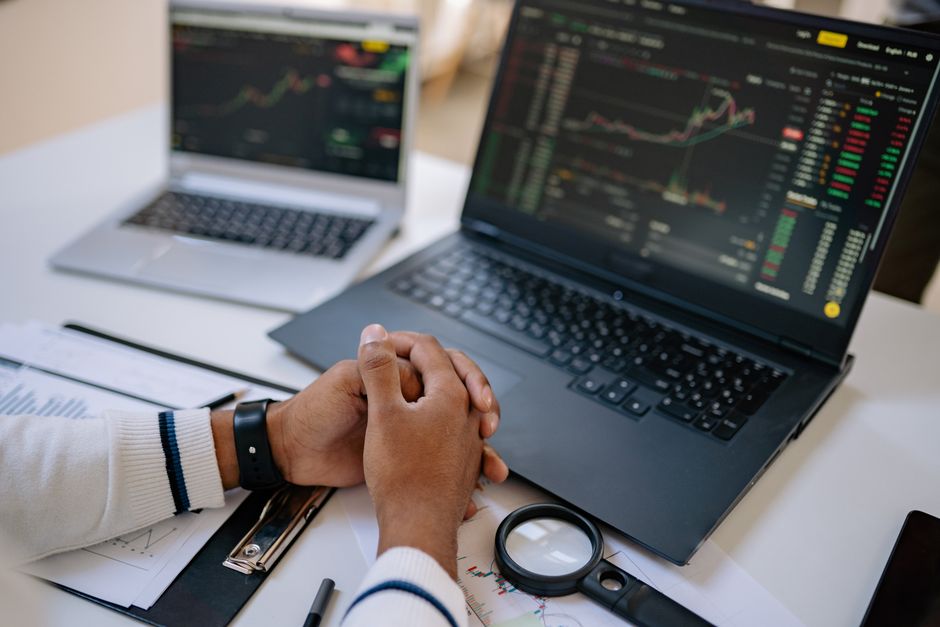 Profitable ESG portfolio — Man seated at a desk using laptops to monitor stock market trends and investments.